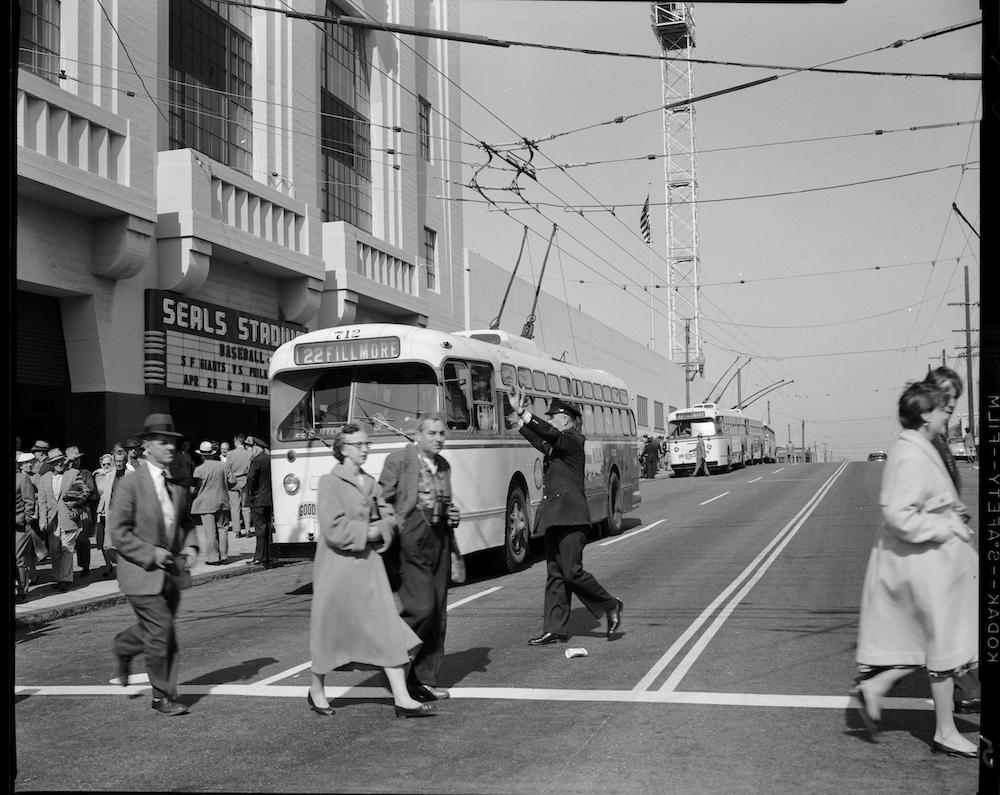 Black and white photo of people crossing the street as a 22 Fillmore bus pauses in traffic.