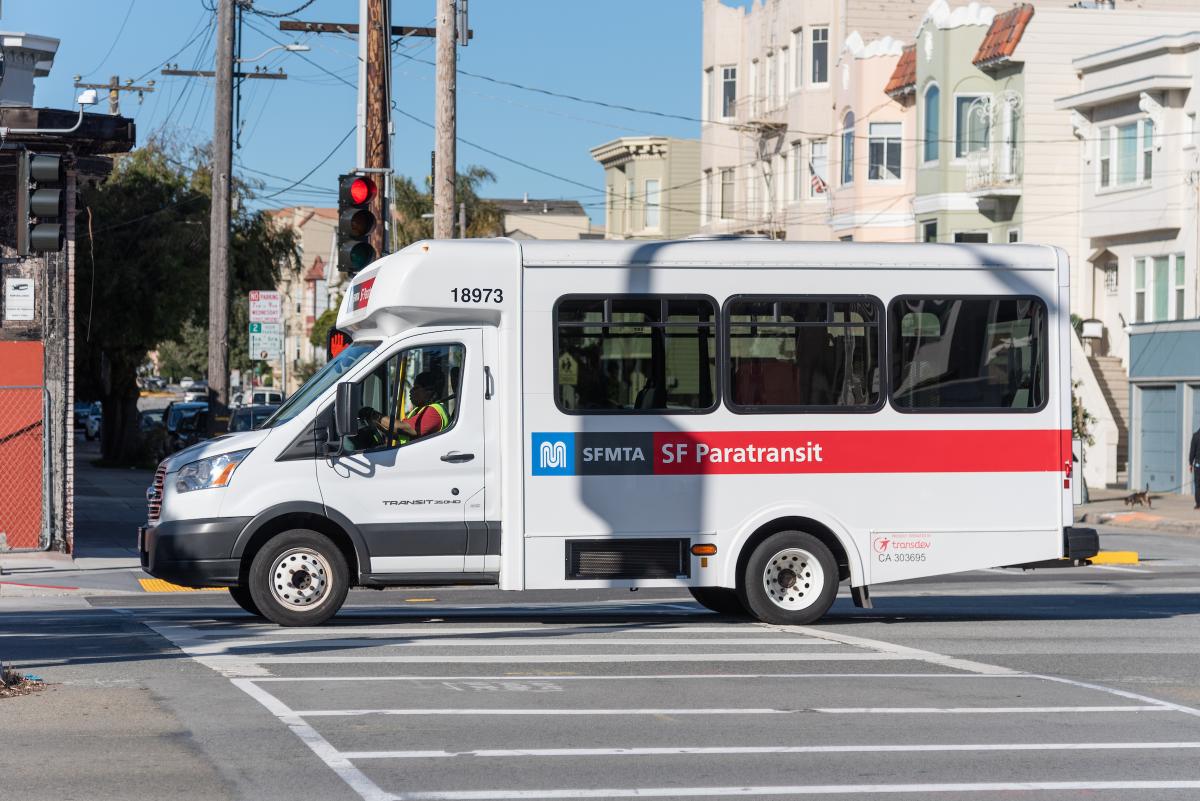 Paratransit vehicle with SFMTA logo drives through an intersection.