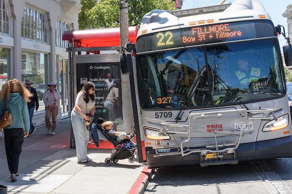 Woman pushes a child in a stroller onto a 22 Fillmore bus.