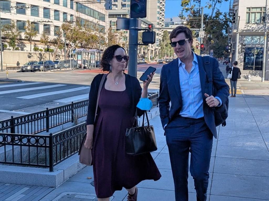 Two people walking on the sidewalk and talking.