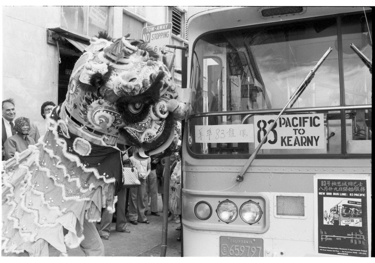 Black and white photo of a dragon costume approaching a bus that says 83 Pacific to Kearny.
