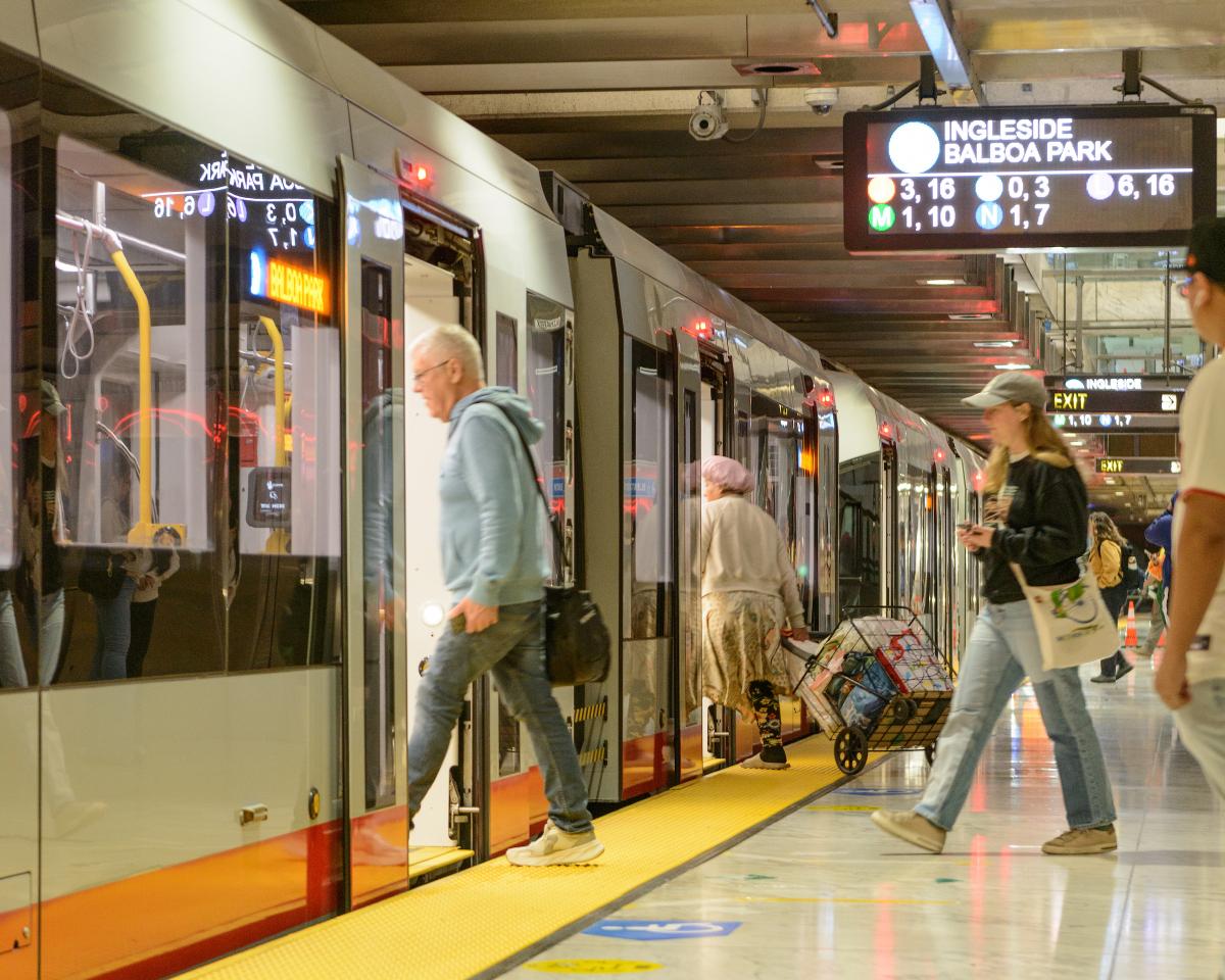 People board a Muni Metro train from a station platform. 