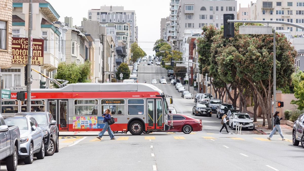 A Muni bus drives on Union Street as people use a crosswalk nearby.