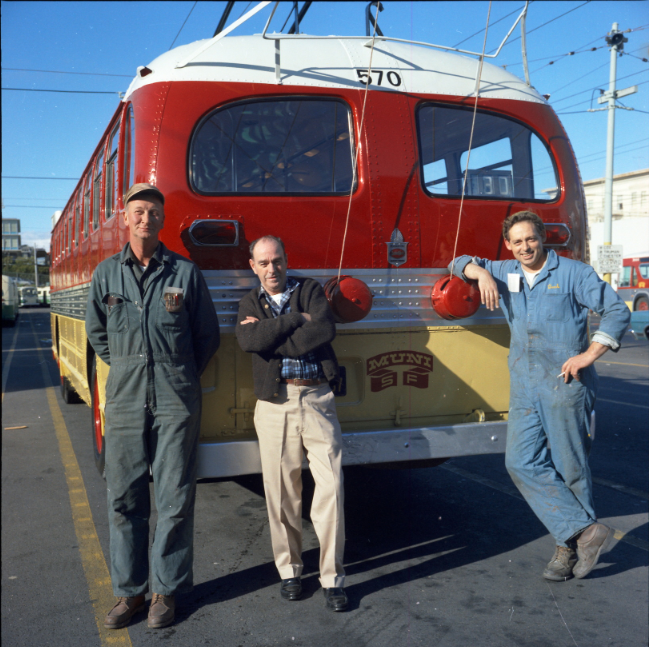Muni staff in Potrero Yard posing by a trolley bus with red and yellow colors. Image from 1970.
