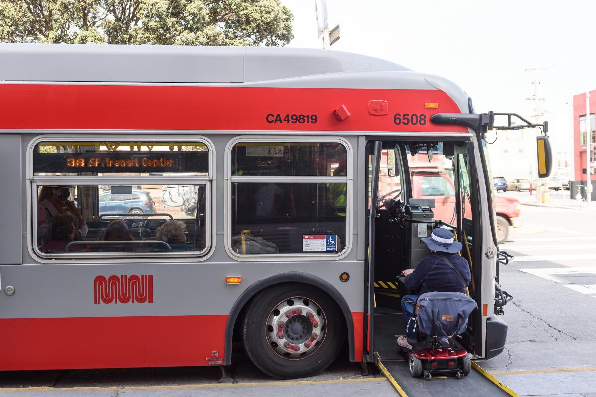 Person using a mobility device boards a Muni bus using a ramp.