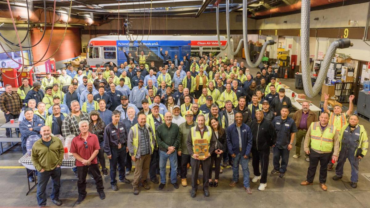 Large group of SFMTA staff in a bus yard. Many wear yellow vests.