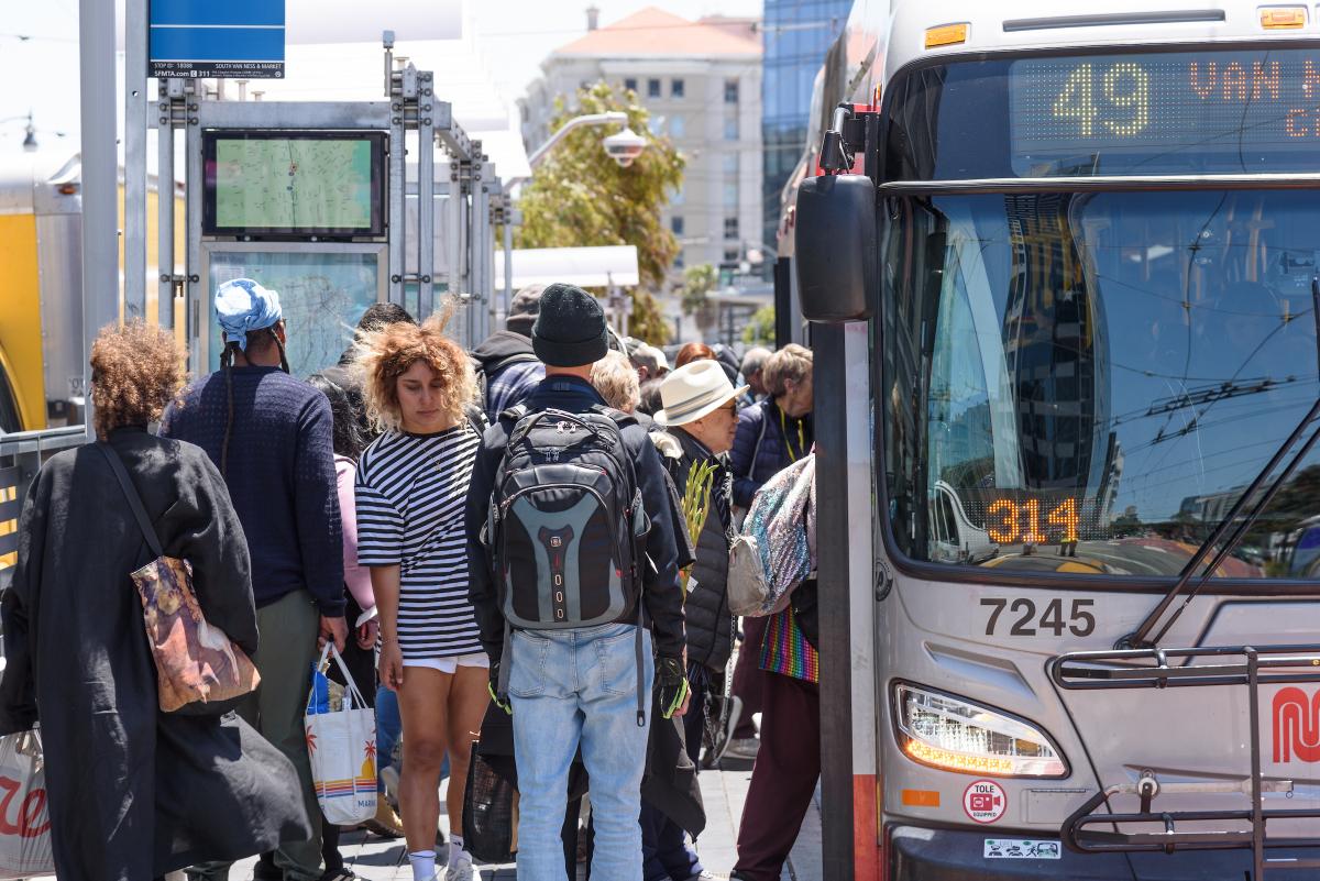 people gather at a bus stop to board a 49 Van ess bus.