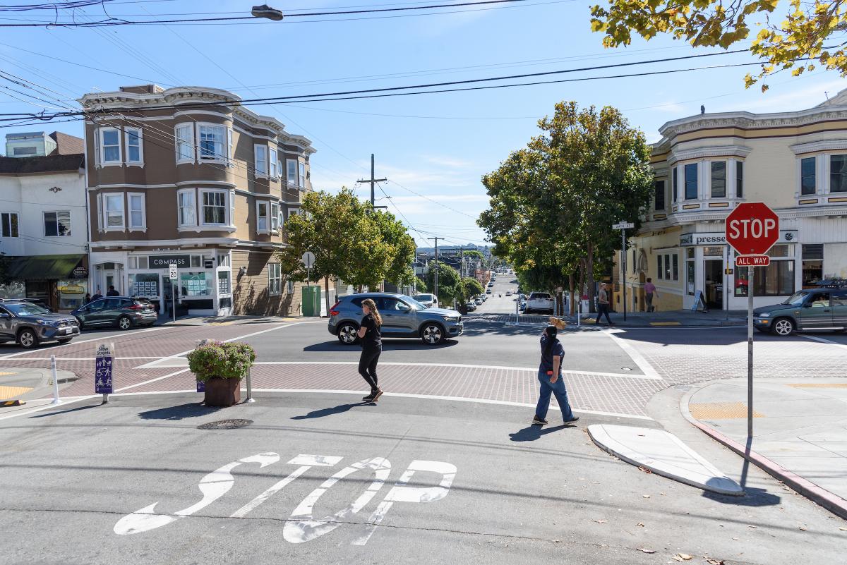 People cross a street in front of small businesses on 24th Street in Noe Valley.