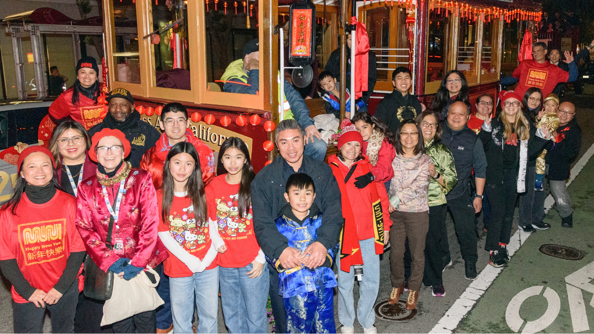 SFMTA staff and young people smile near a cable car as part of a Chinese New Year Parade event.