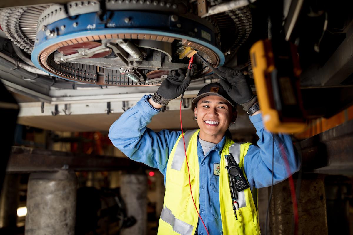 SFMTA mechanic wearing a yellow vest smiles while repairing a vehicle.