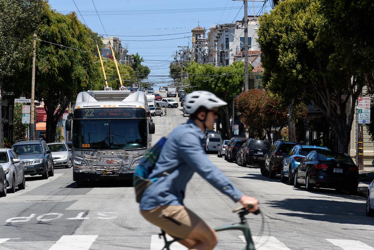 Person riding a bike with the 22 Fillmore bus in the background. 
