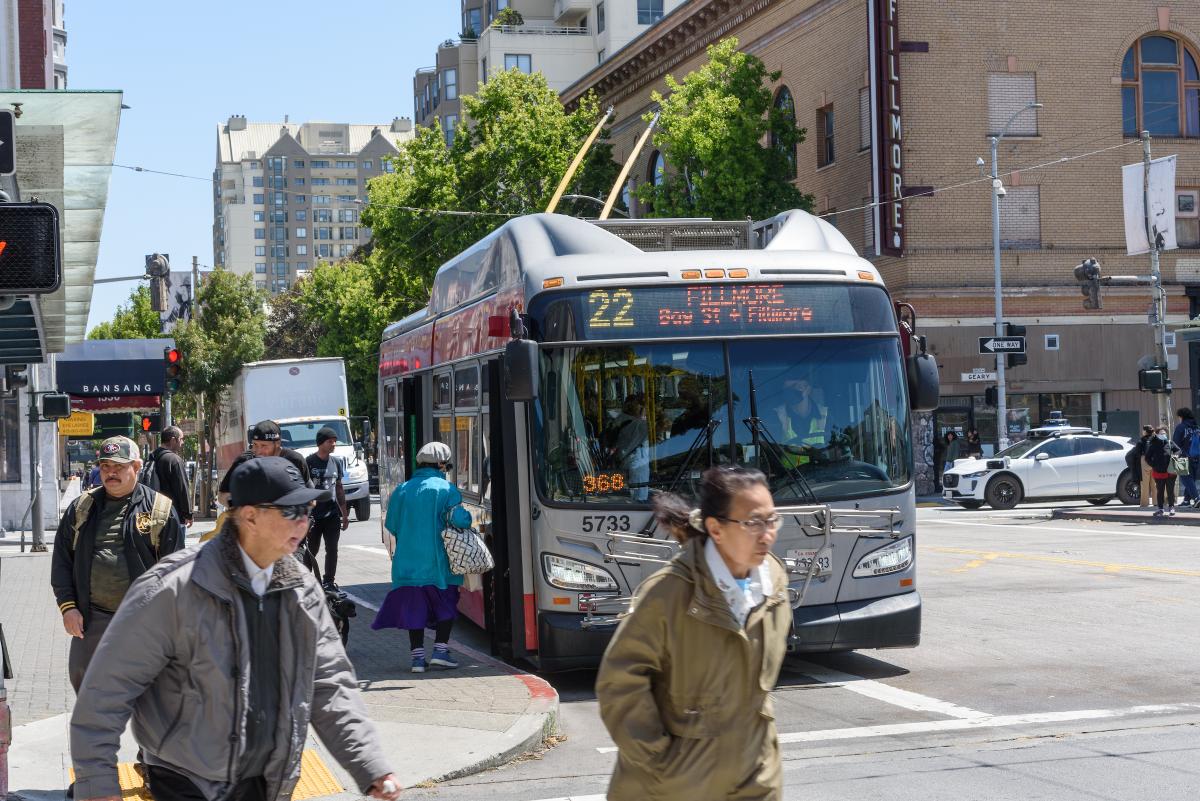 People boarding and walking near one of Muni’s electric trolley buses.