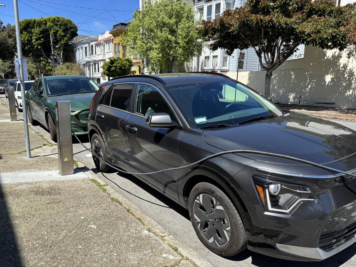 Two cars at the curb connected to charging machines.
