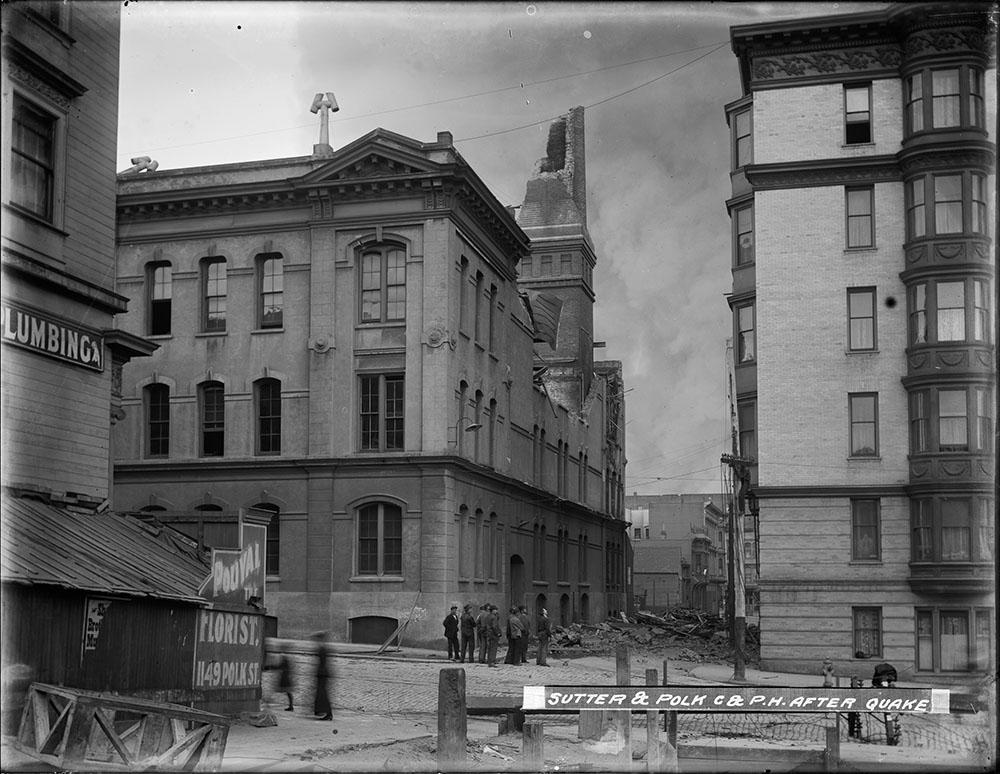 People standing on a corner near rubble from a damaged building