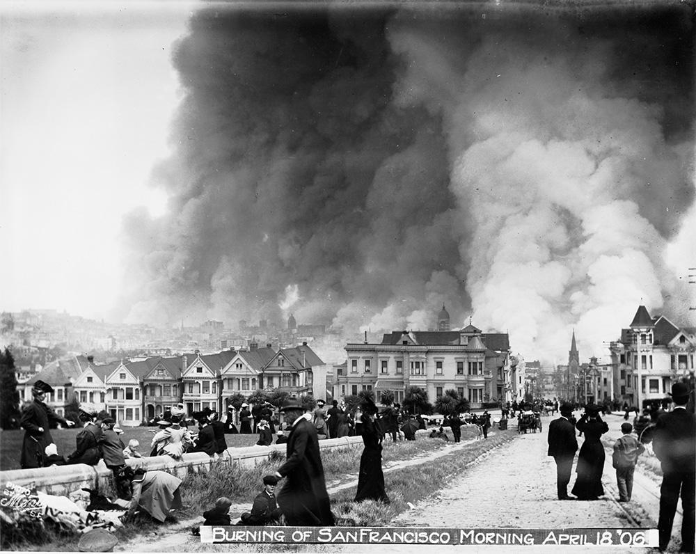 People standing near buildings with smoke nearby  