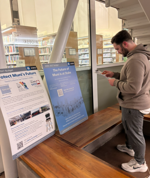 A person at an SFMTA pop-up open house in a library looking an information signs.