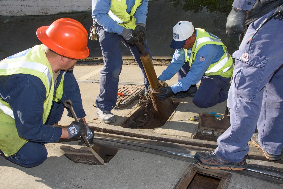 Four people in safety gear hover over a Muni track switch during a Fix It! event.