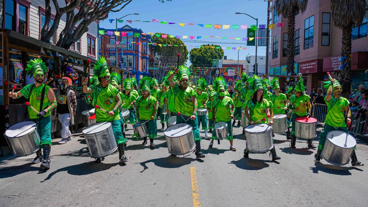 People in costumes beating large drums in a parade.