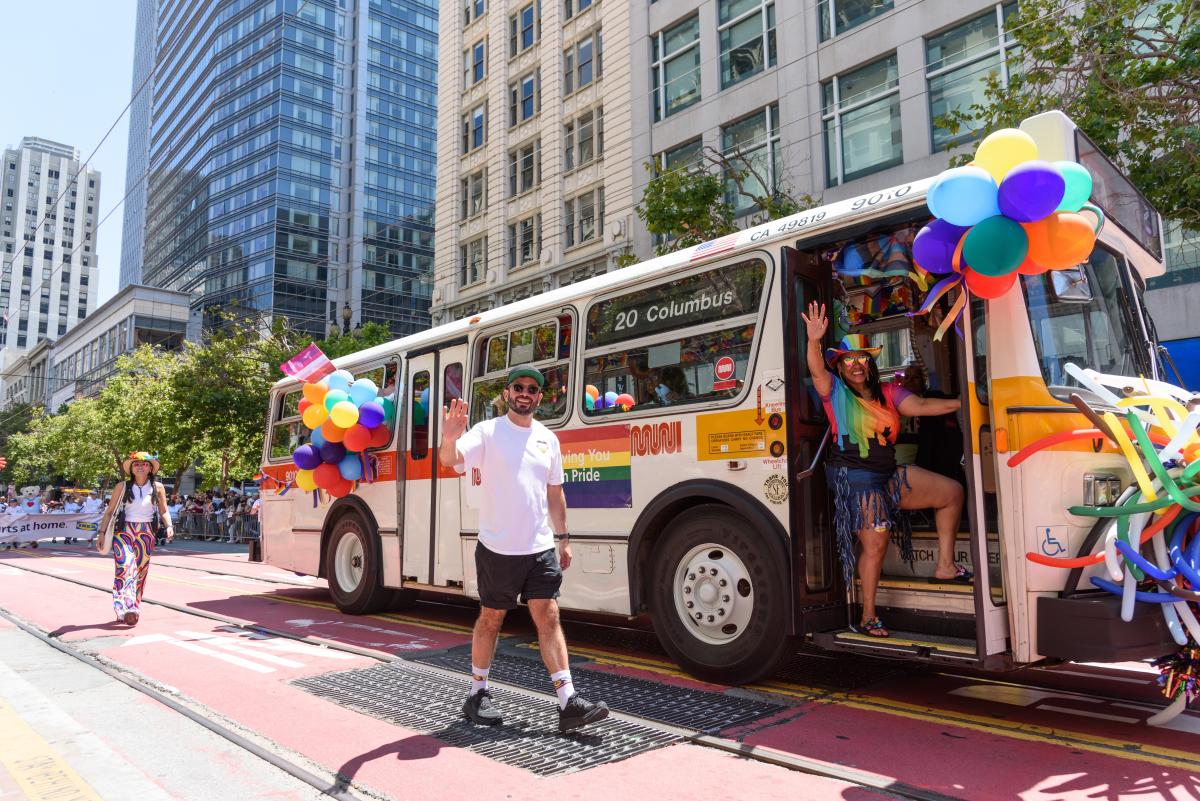 People walking in the street and riding a bus decorated with ballons