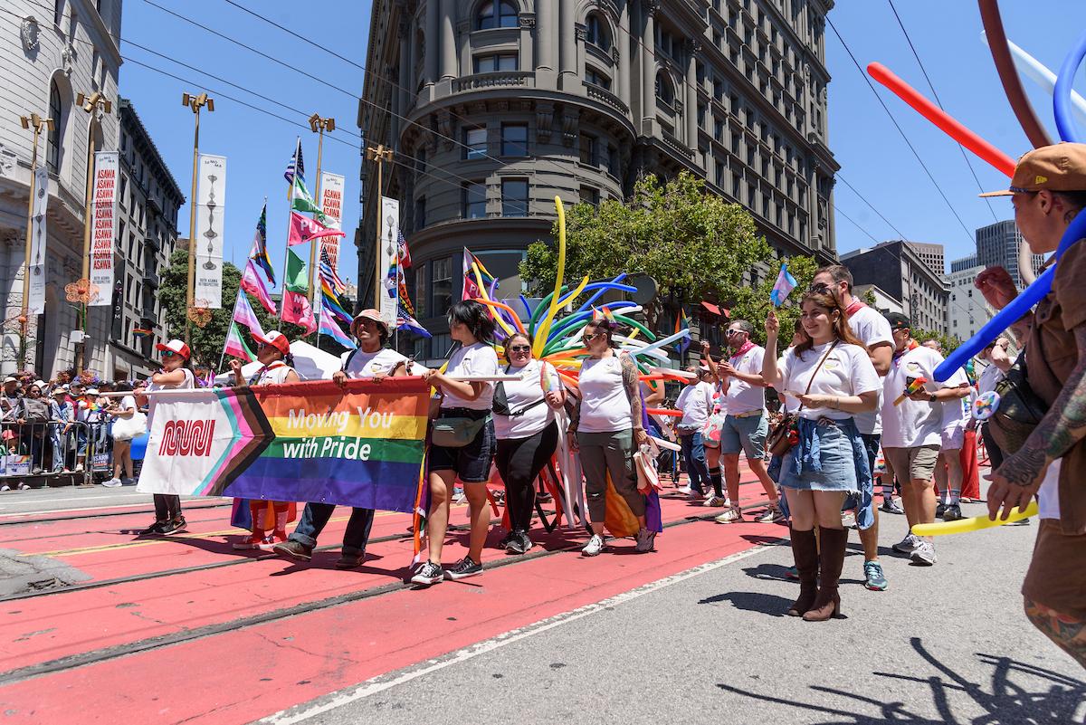 SFMTA staff marching on Market Street with a banner says “Moving you with Pride” at the San Francisco Pride Parade.