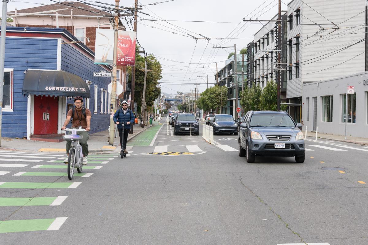  People riding an e-bike and scooter in a bike lane.