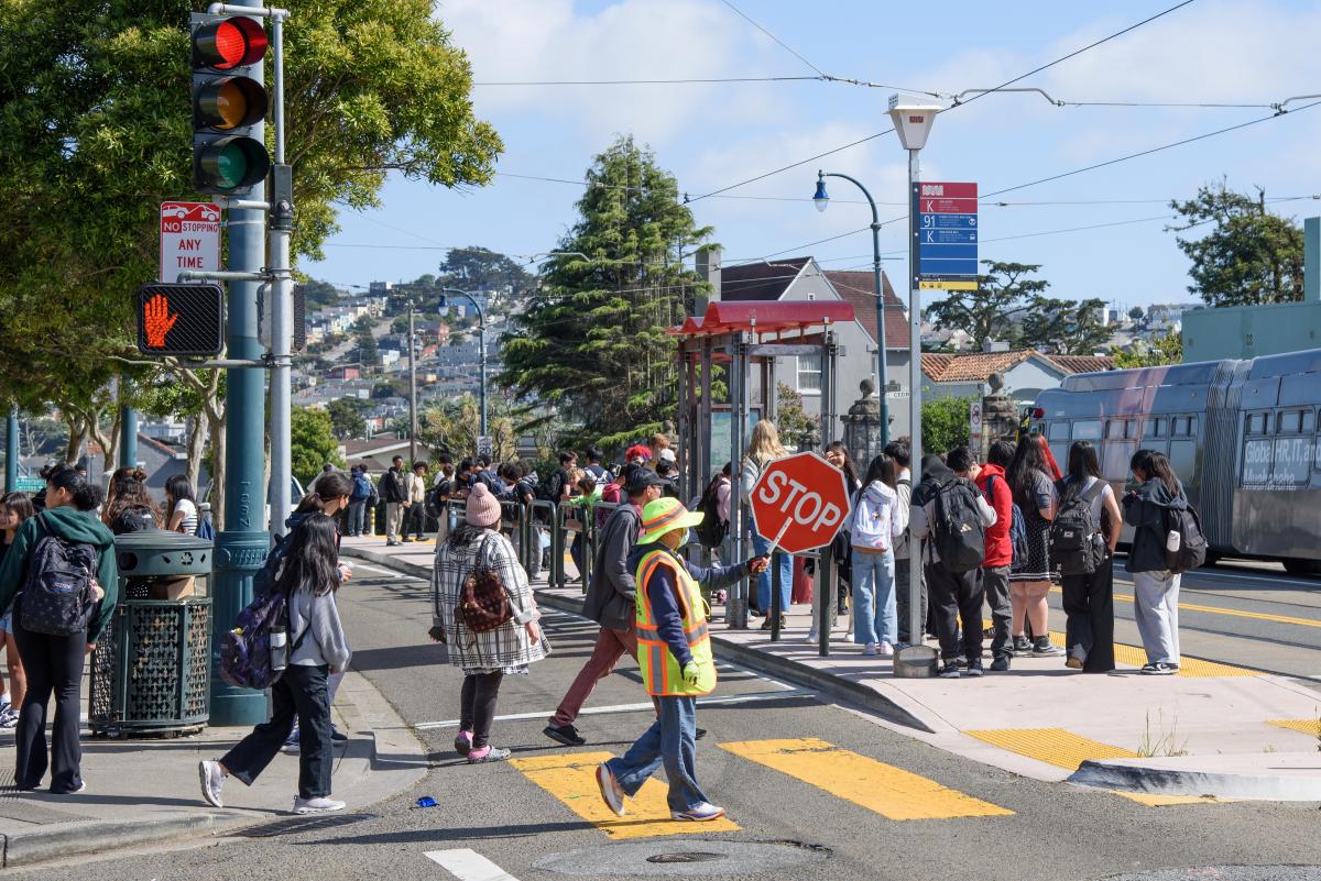 People walking through a crosswalk and waiting at a bus stop.