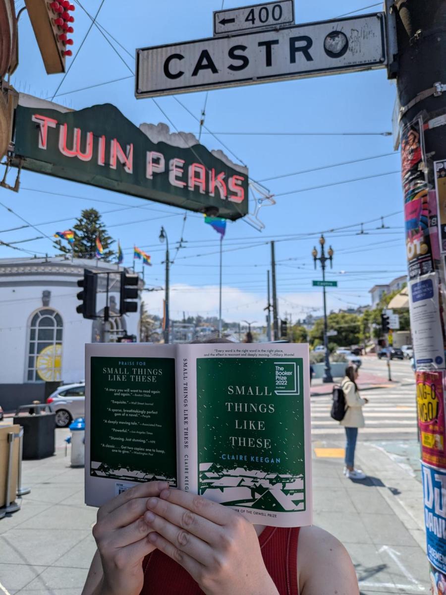  A person holds a copy of Claire Keegan’s “Small Things Like These” in front of the Castro street sign and Twin Peaks Tavern on a sunny day in San Francisco. 