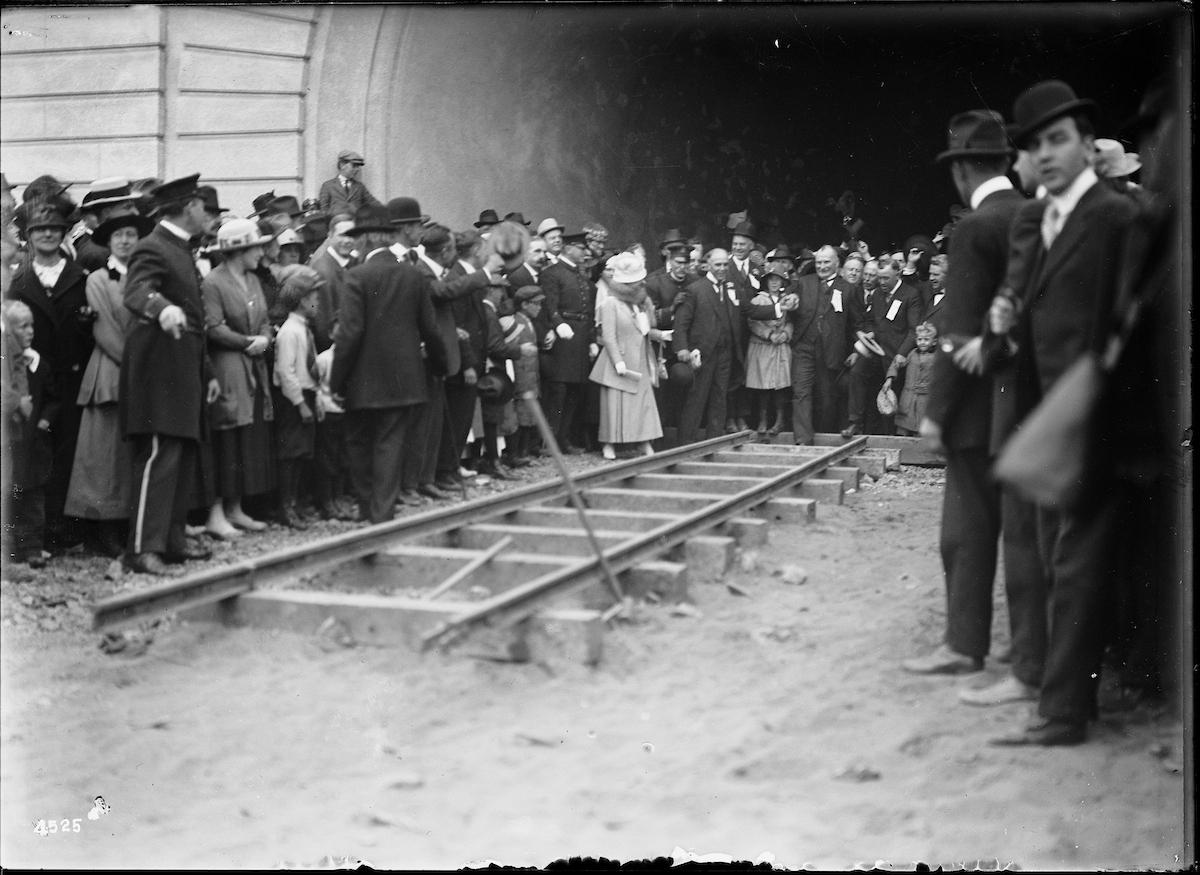 Black and White Photo of Mayor James Rolph and City Engineer Michael O'Shaughnessy preparing to drive a Ceremonial Silver Spike for the First Track Laid at the West Portal of the Twin Peaks Tunnel on Day of Tunnel Dedication with Large Crowd | July 14, 1917 