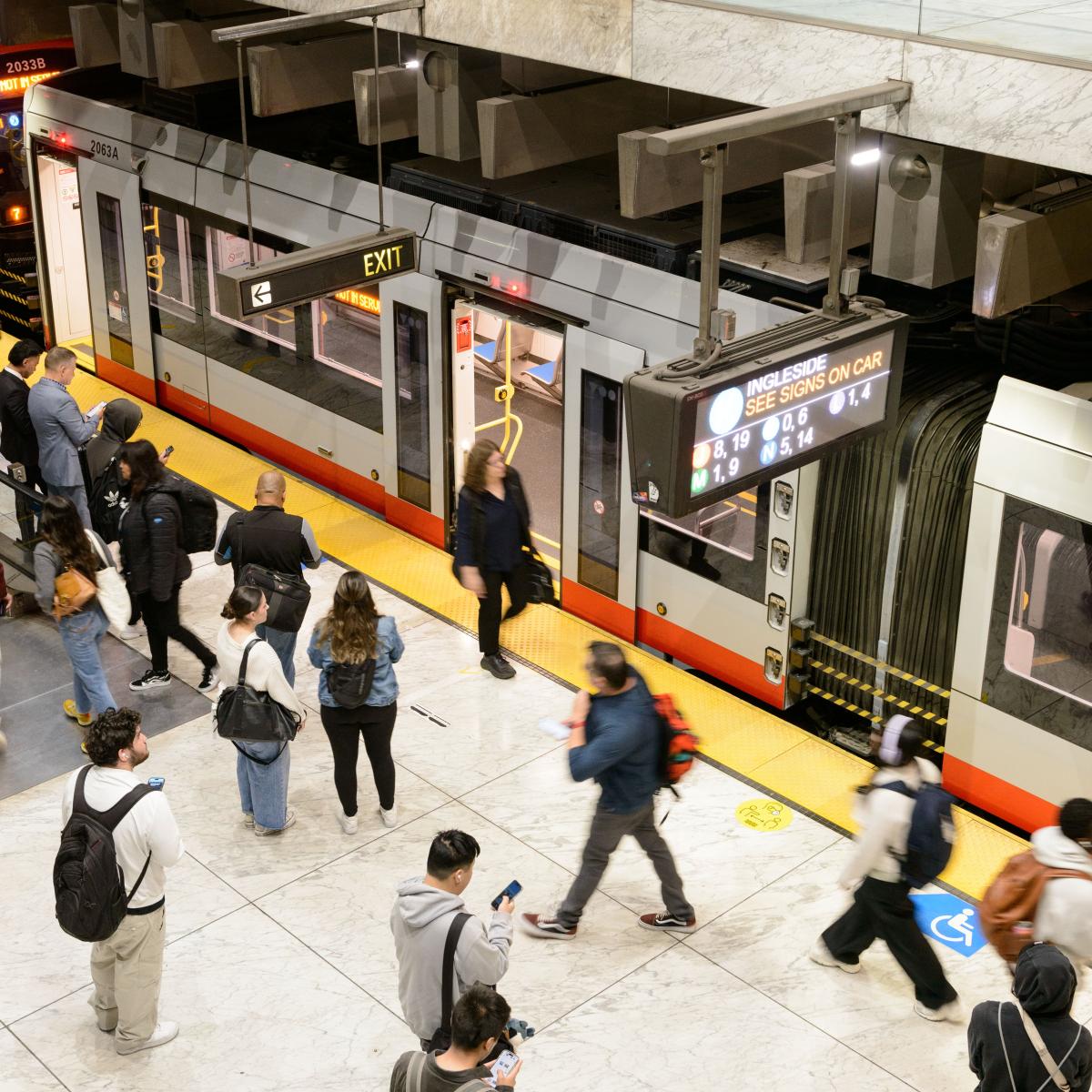 people walk around a metro station while a train pulls in 