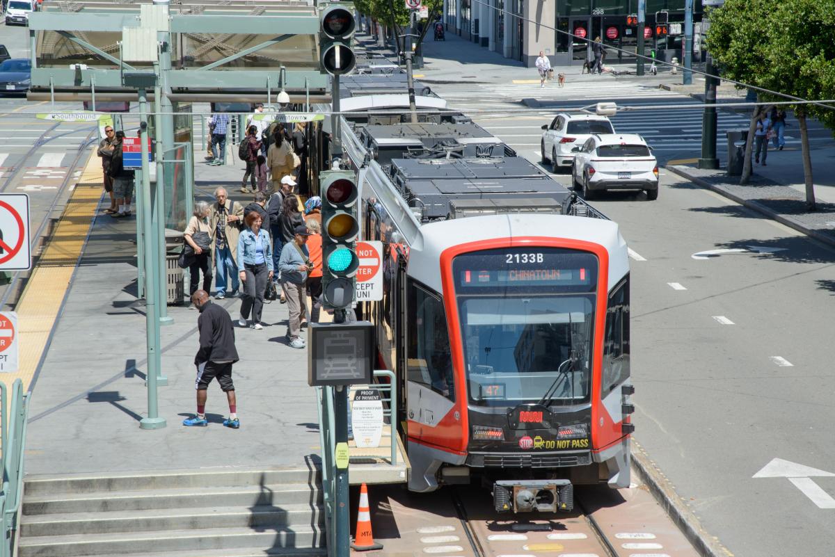 A crowd of people wait on a transit platform and board a Muni train