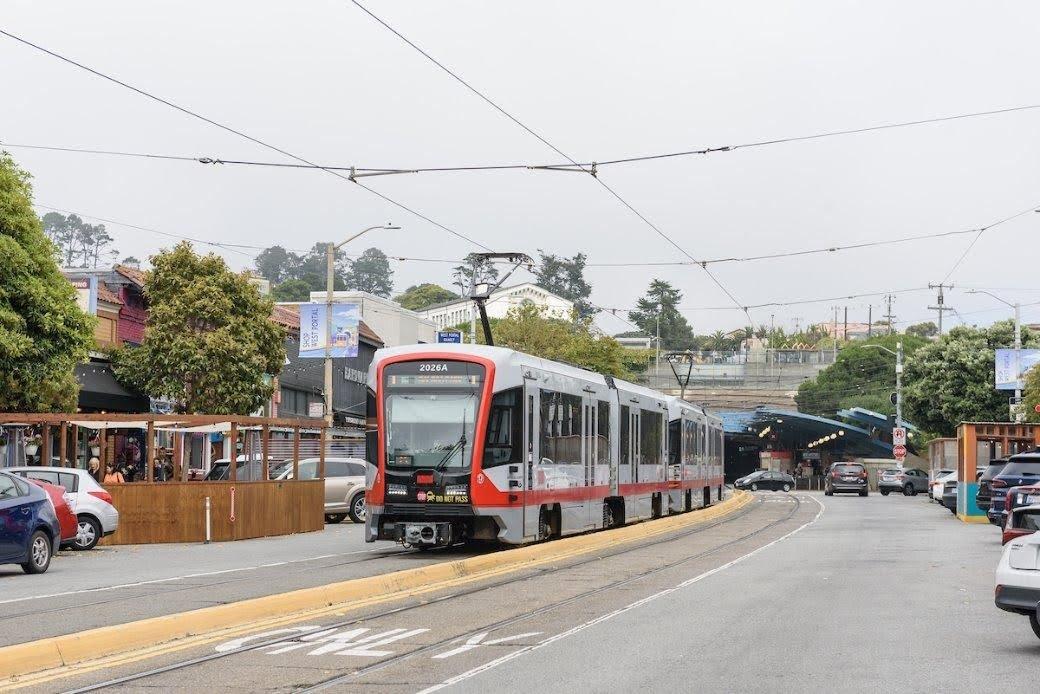A train travels down a street with parked cars. 