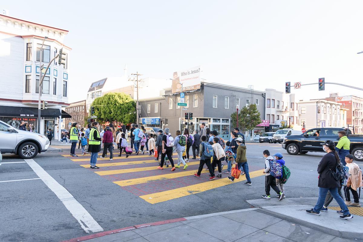 Young people walking in a crosswalk that’s guarded by crossing guards.