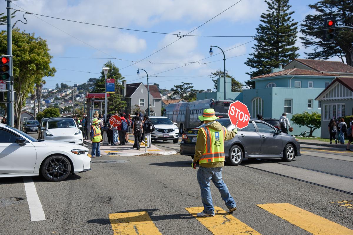 Crossing guard, cars and pedestrians in an intersection.