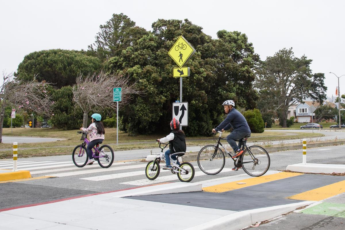 An adult and children riding bikes through a crosswalk.