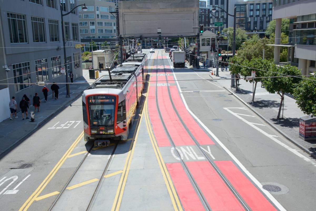 A light-rail vehicle traveling down the street next to a red transit lane.