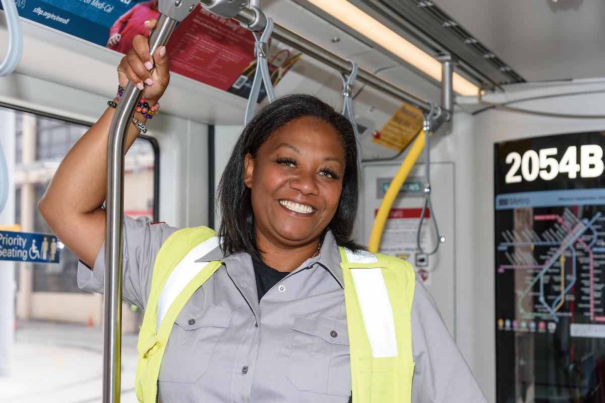 A woman in a grey shirt and bright yellow vest standing on a transit train
