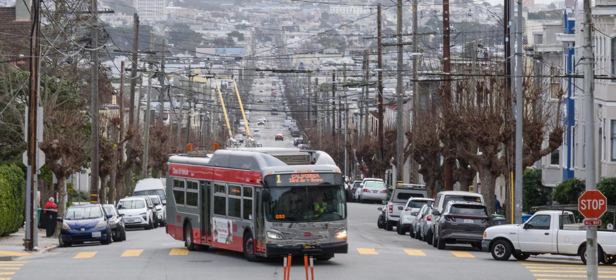 A bus drives down the street with parked cars on either side