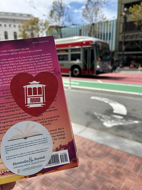 A book featuring a Muni sticker is shown in front of an oncoming bus.