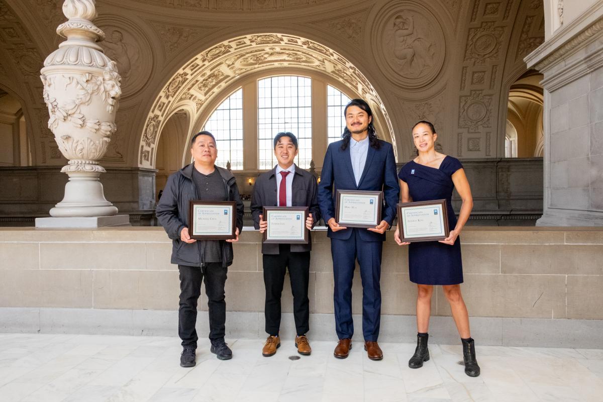 Four people standing in a line holding framed certificates.