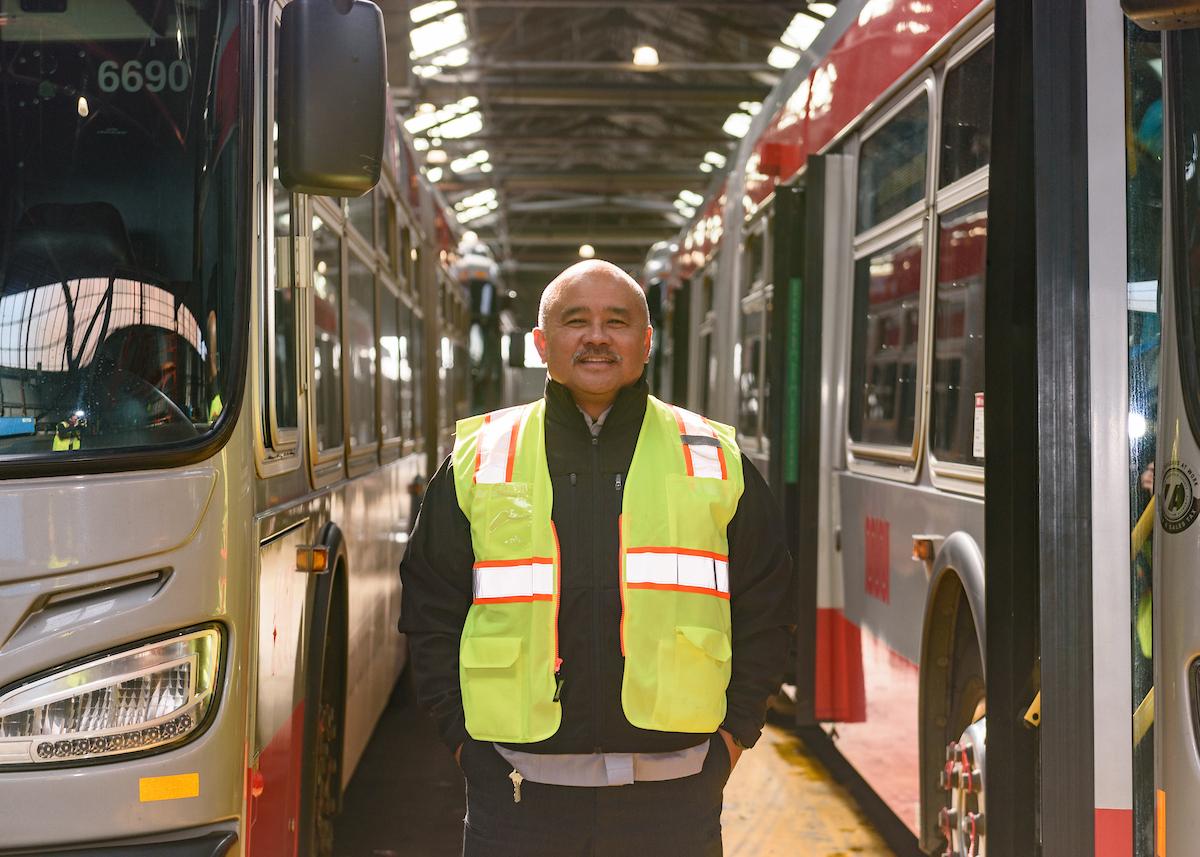 A person wearing a yellow vest and standing between two buses.