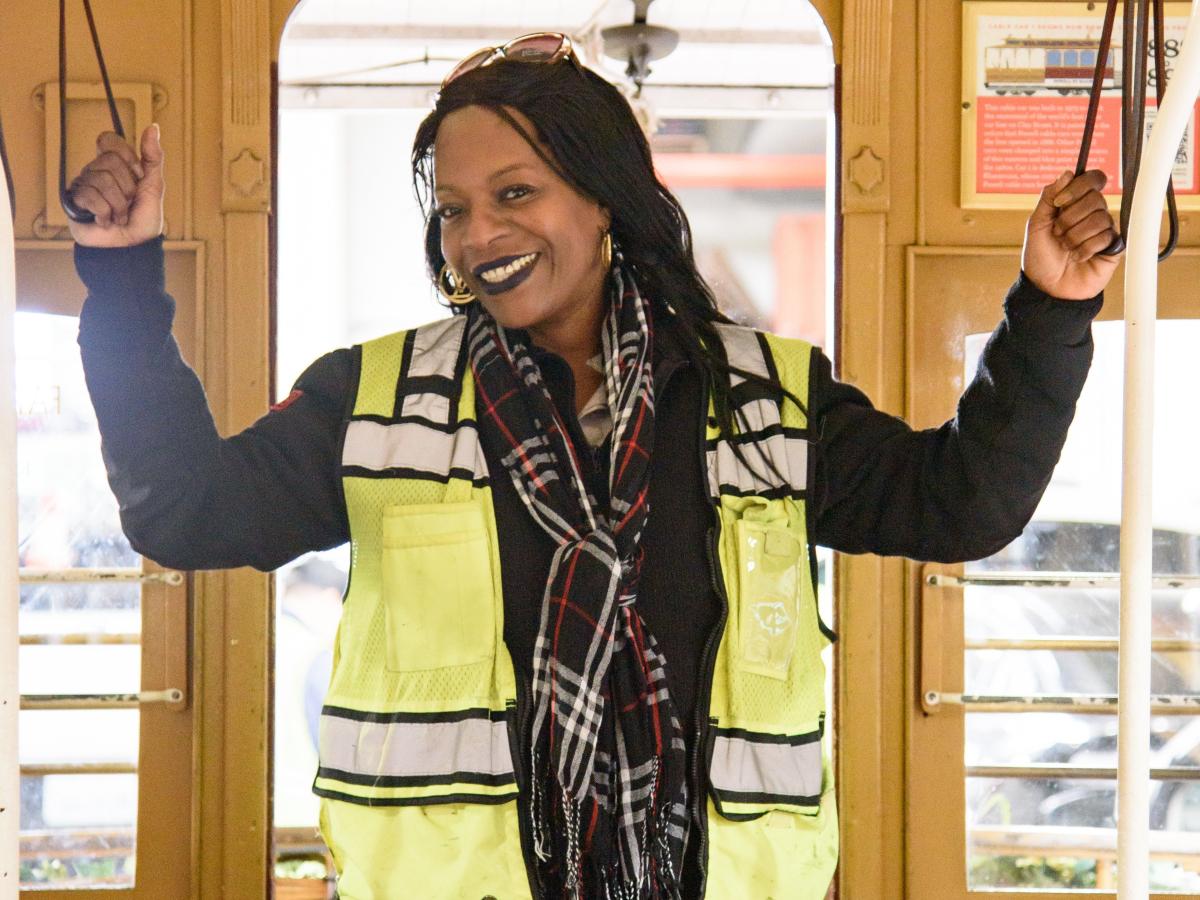 A person wearing a yellow vest standing on a cable car with her arms raised.