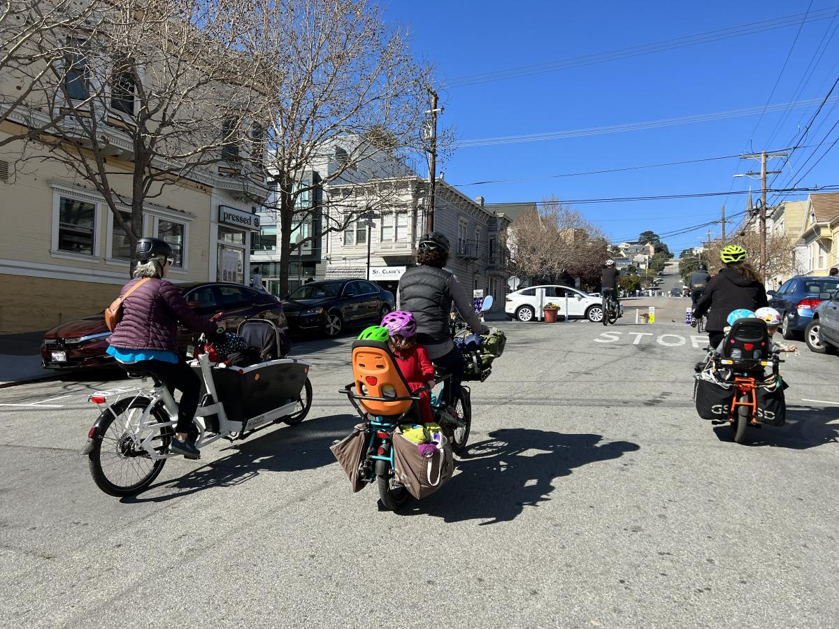 Adults and small children riding electric bikes in a street