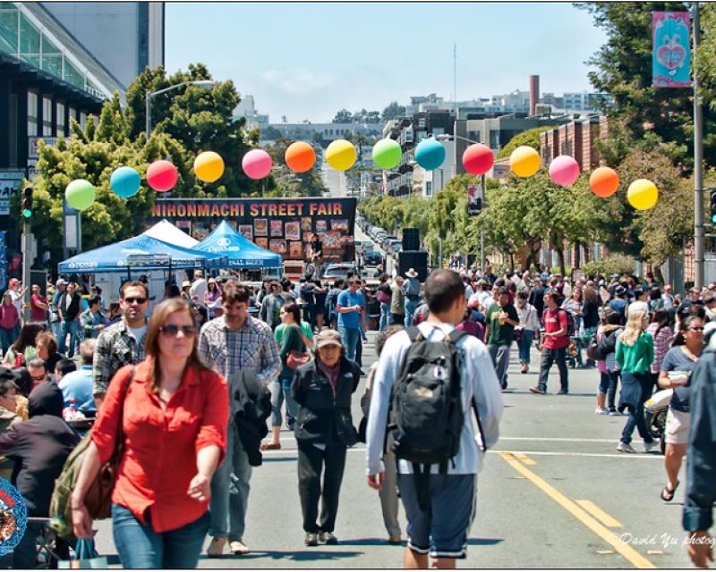 People out enjoying a street fair under a bright afternoon sky.