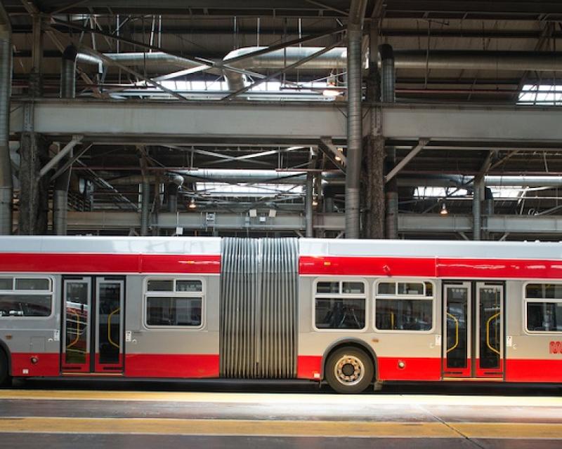 A 60-foot Muni bus parked in a garage with its front door open.