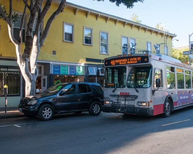 Outbound 48 Quintara-24th Street bus driving past a yellow building in the afternoon.