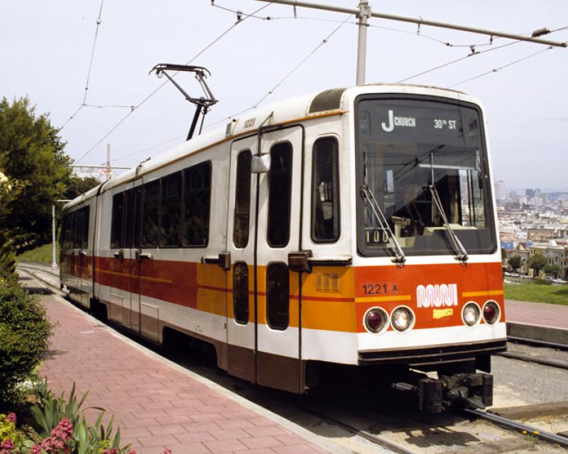 color photograph showing a Muni Boeing LRV climbing the hill in dolores park in the 1980s.  The car is stopped near the top of the hill with a view of the city skyline behind it.