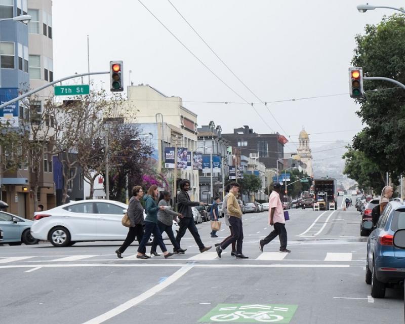 People and car traffic cross Howard Street at 7th Street. Howard has three traffic lanes, a bike lane and two parking lanes.