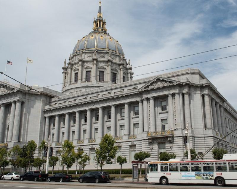 San Francisco City Hall viewed from Van Ness Avenue, with cars and a Muni trolley bus on the street.
