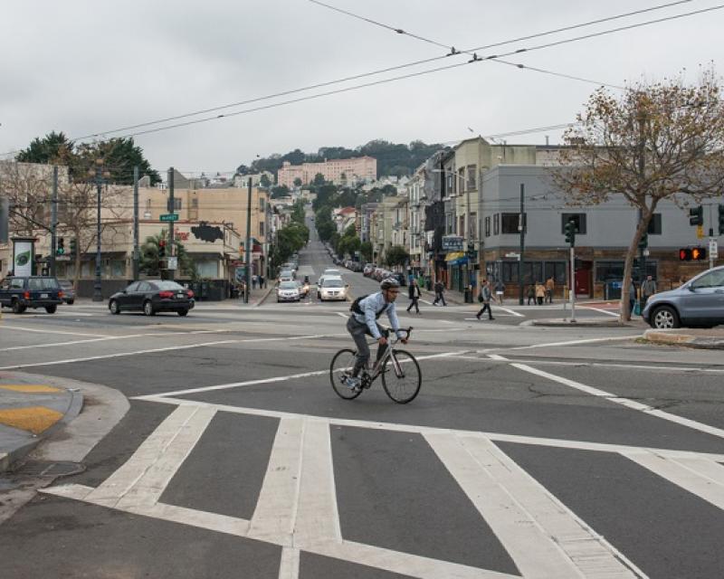 Daytime view looking west on 14th Street at its intersection with Market and Church streets with people walking, driving and a man bicycling.