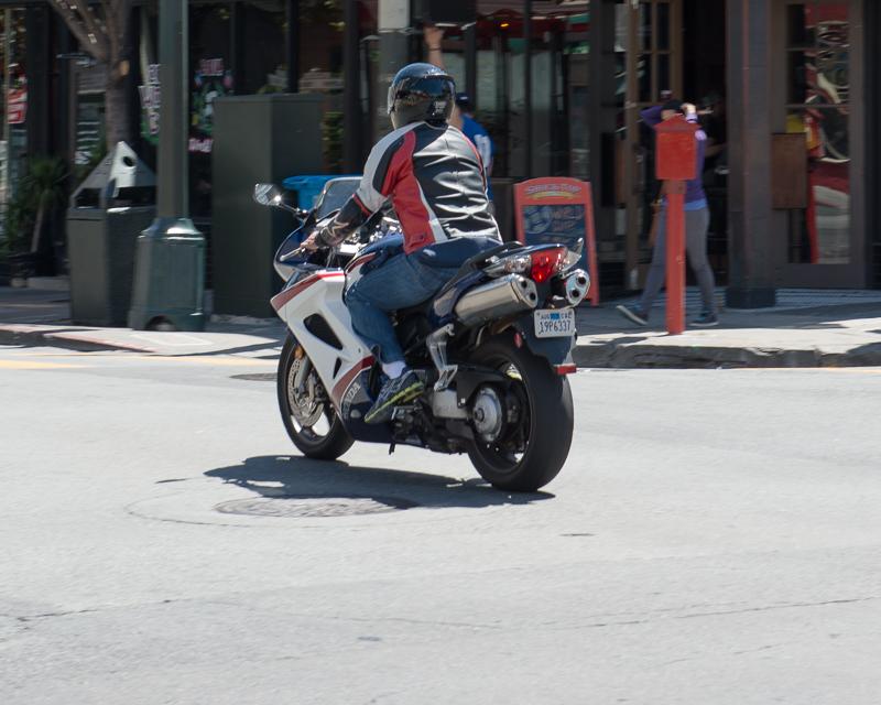 person on motorcyle wearing red, white,a nd black leather jacket traveling through intersection